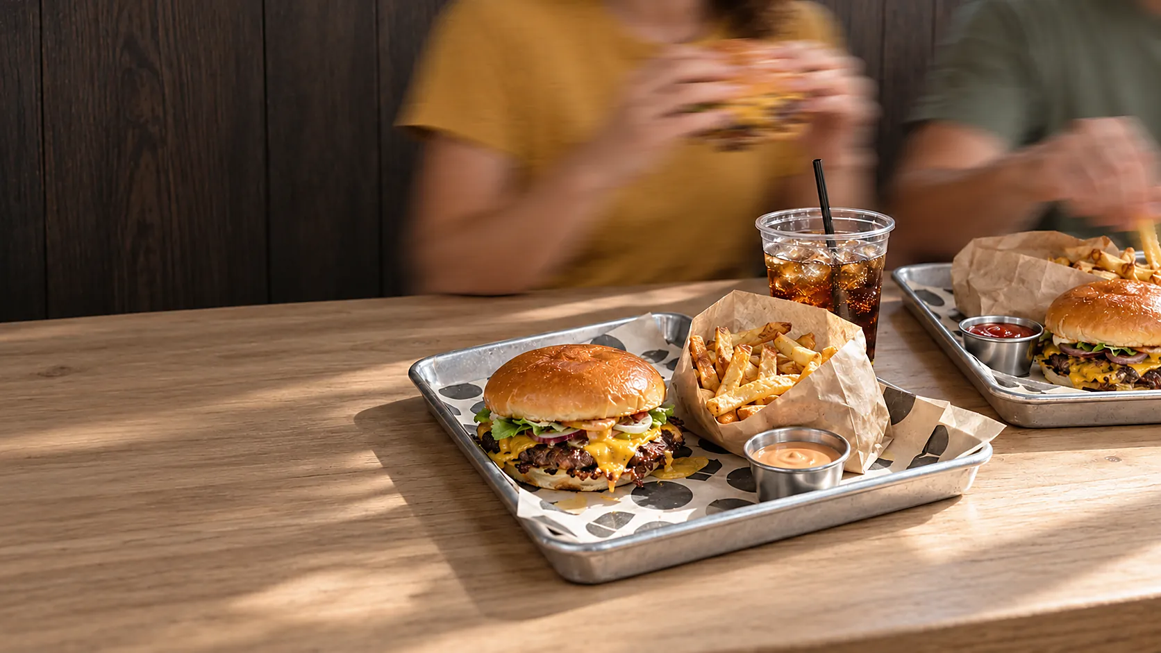 Dos personas comiendo hamburguesas con papas fritas y bebidas en la mesa de un restaurante
